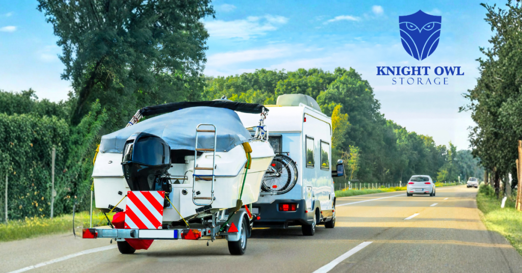A motorhome towing a covered boat on a trailer down a highway under a clear blue sky